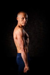 A muscular tattooed man on a dark background.