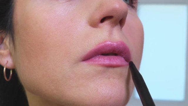 Applying pink lipstick to lips