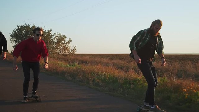 Three happy hipster men skateboarding at empty road at sunset rapid slow motion