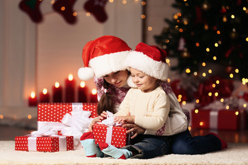 Fototapeta na wymiar Beautiful two sisters with gift boxes sitting near christmas tree at home