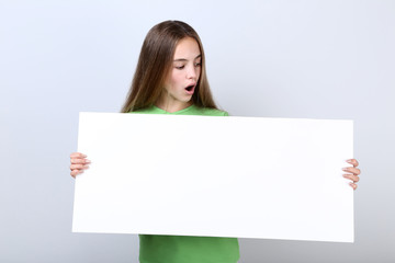Surprised young girl holding blank board on grey background