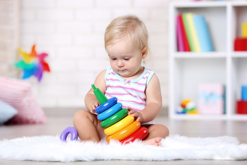 Baby girl sitting on white carpet with toy