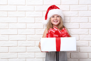 Little girl holding gift box on brick wall background