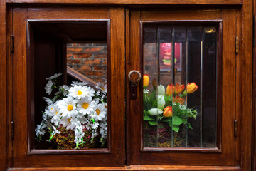 Two bunches of artificial flowers in old wooden cabinet. Interior decoration