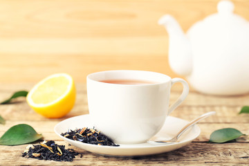 Cup of tea with green leafs and lemon on wooden table