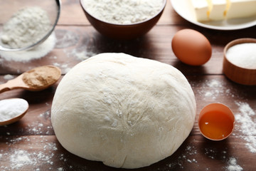 Raw dough with eggs and flour on wooden table