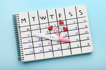 Pregnancy test with paper calendar and red hearts on blue background