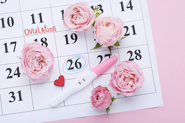 Pregnancy test with rose flowers on paper calendar