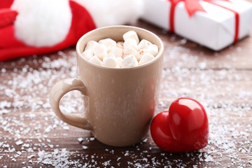Cappuccino with marshmallows in cup and red heart on wooden table