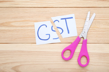 Paper with word GST and scissors on wooden table