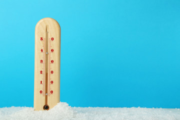 Wooden thermometer in snow on blue background