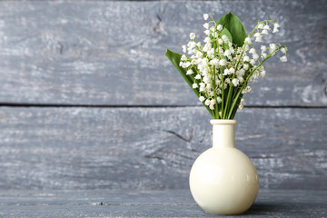 Lily of the valley flowers in vase on grey wooden table