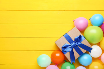 Colorful balloons with gift box on yellow wooden table