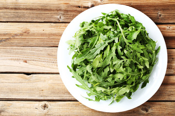 Green arugula leafs in plate on brown wooden table