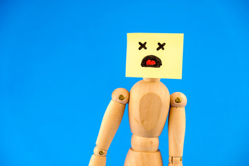 Abstract image with a wooden dummy with sticker with shocked face on blue background.