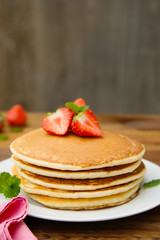 Delicious homemade american pancakes with fresh strawberry and honey. Wooden rustic background.