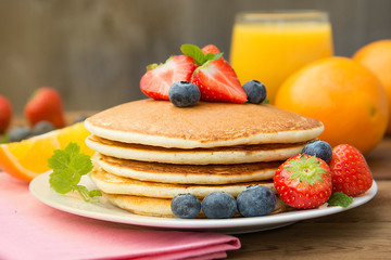 Homemade american pancake with fresh blueberries, strawberries and orange juice. Wooden rustic background.