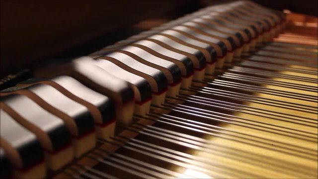 Hammers hitting the strings inside of a grand piano while the pianist plays Bach