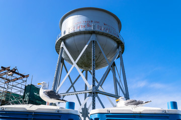 Water Tower On Top Of Green Hill, Backlit By Sun Against Blue Sky, Alcatraz Island