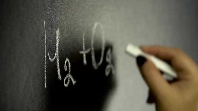 Girl writing chemistry formula on black board