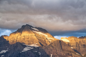 The Rocky Mountains win Glacier National Park with early morning light and stormy clouds overhead.