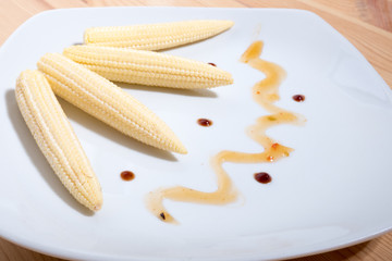 four raw cob mini corn on a plate decorated with sauce. Horizontal photo format