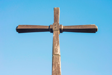 Concept or conceptual wood cross or religion symbol shape over a blue sky. Simple wooden Christian cross against a blue sky