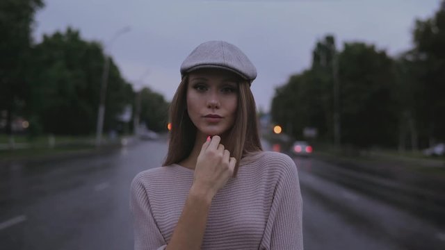 beautiful girl in a cap stands on an empty road in the city. look into the camera