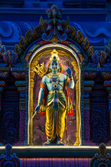 A nighttime image of an Indian deity lite up while standing in an arch.
