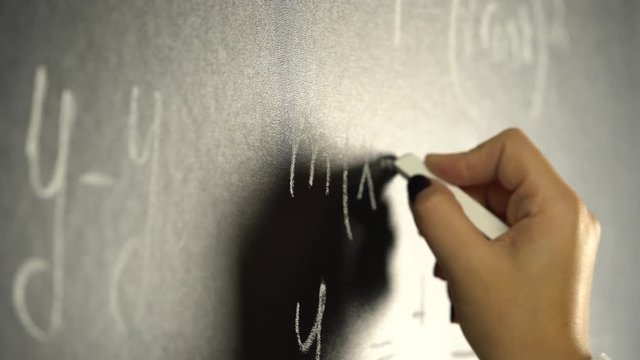 Hand is writing with a chalk a mathematical of a formula on a blackboard