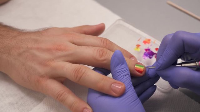 Close-up of manicurist drawing a six-band rainbow LGBT flag on the man fingernail.