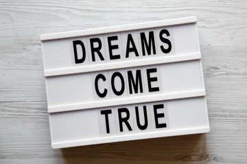 'Dreams come true' words on modern board over white wooden background, overhead. Top view, flat...