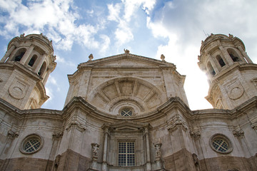 Look up at the facade of the Cathedral of Cadiz in Spain with the sun peaking from behind one of the bell towers.