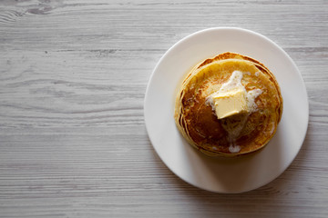 Homemade pancakes with butter on white plate over white wooden background, overhead view. Space for text.