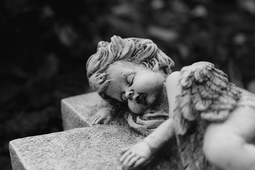 Black and white image of putto or child angel figurine sleeping on a cross