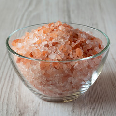Fototapeta na wymiar Himalayan sea salt in a glass bowl on white wooden surface, side view. Closeup.