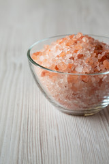 Himalayan sea salt in a glass bowl on white wooden background, side view. Close-up.