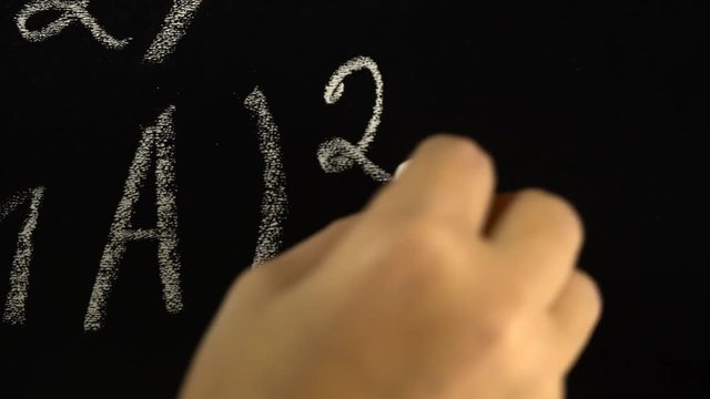 Hand writing with chalk the algebra formula on the blackboard. Close up