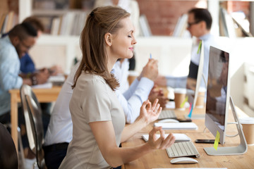 Calm relaxing businesswoman doing yoga exercise, meditating at workplace in front of computer, resting after long work, no stress, breathing deeply, relief, taking break, pause, healthy good habits