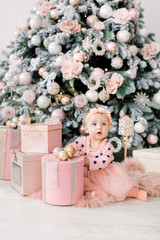 cute little girl in bklom dress sitting in the flour and opens a box with a present for background Christmas tree . Xmas holiday concept