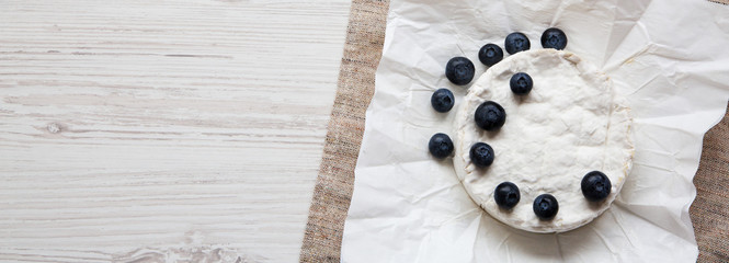 Camembert cheese in paper on a white wooden background, overheadview. Food for wine. Copy space.