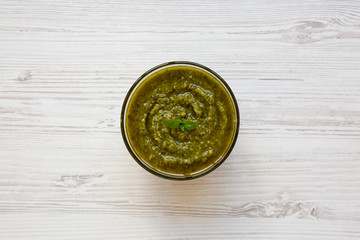 Bowl of freshly made basil pesto on white wooden background, top view. From above, overhead.