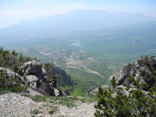 Beautiful mountain landscape with top view of a distant valley with lake. Distant mountain plateaus in a blue haze. Crimean mountains.