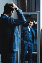 Perfect look. Reflection of handsome young man in full suit adjusting his jacket while standing in front of the mirror indoors.
