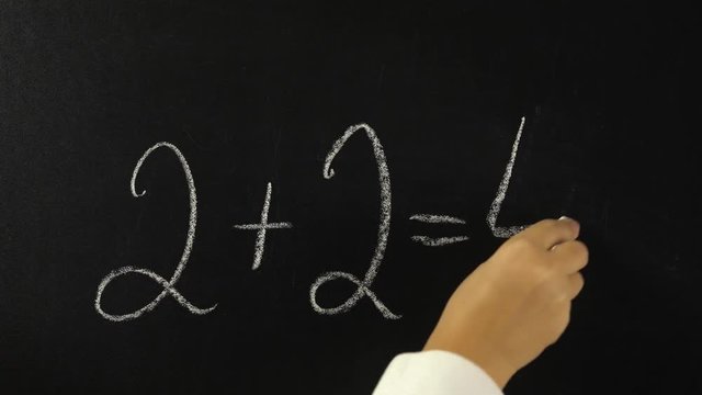 Hand writing with chalk on chalkboard mathematical equation, two plus two equals four