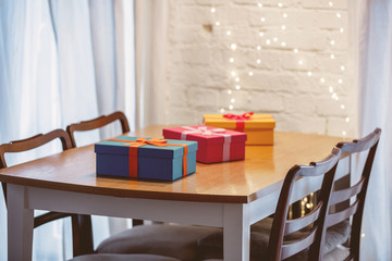Colored gift boxes on table with Christmas lights on background