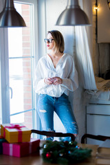 Young caucasian woman in white shirt and blue jeans with glass of a wine stay in a kitchen.