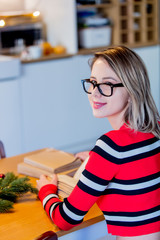 Adult caucasian girl in red sweater with books sitting at table with Christmas decoration at home.