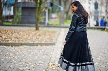 Pretty indian girl in black saree dress and leather jacket posed outdoor at autumn street.