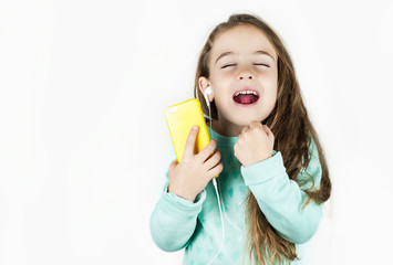 Bright beautiful little girl in headphones with a phone in her hands emotionally talks and rejoices on an isolated background.